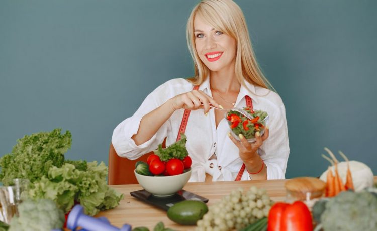 Blonde woman enjoying a fresh salad surrounded by vegetables, promoting healthy eating.
